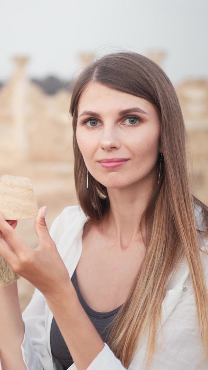 Una bella donna con lunghi capelli castani che indossa una camicia bianca in posa all'aperto.