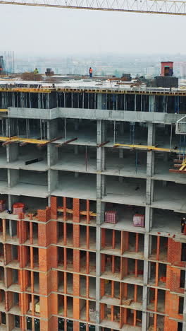 massive residential building at construction site. drone aerial view of new development with cityscape. wide view of a new building with urban city behind. vertical video