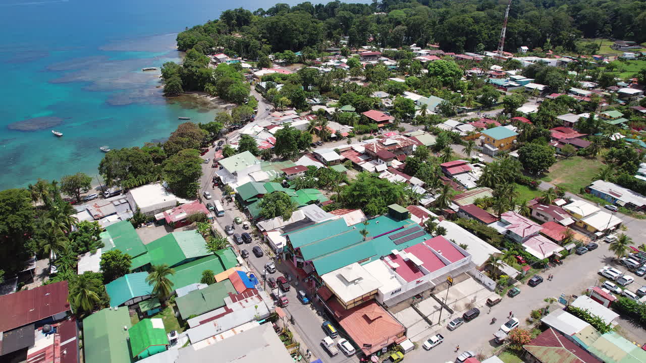 An aerial flying over downtown Puerto Viejo, a tropical Central American tourist destination in Costa Rica, with coral reefs and fishing boats in the bay by the lush and scenic beach.