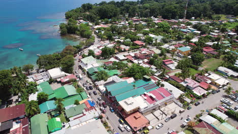 an aerial flying over downtown puerto viejo, a tropical central american tourist destination in costa rica, with coral reefs and fishing boats in the bay by the lush and scenic beach.