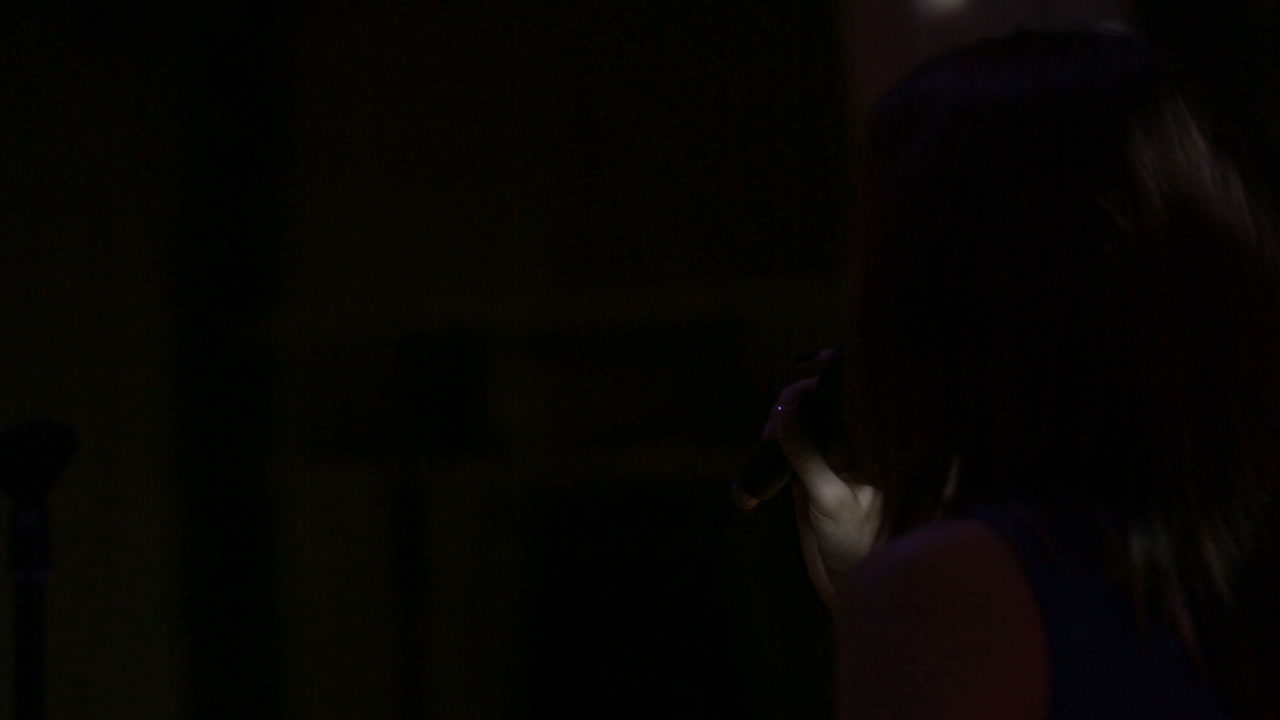 Young pretty woman singing in microphone on dark stage