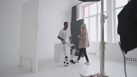 a female make-up artist makes makeup at a professional photo shoot of a football player. photo studio with professional equipment and team of workers. team discussing direction for production