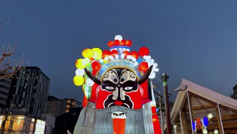 large traditional japanese mask display with lanterns at dusk, vibrant cultural event