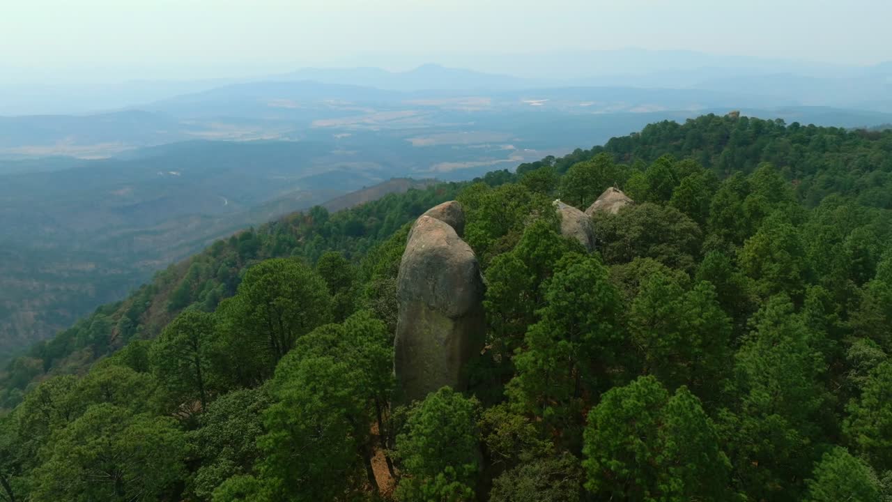 Drone view of massive stone monoliths rising from dense pine forest in Los Frailes, Tapalpa, Jalisco