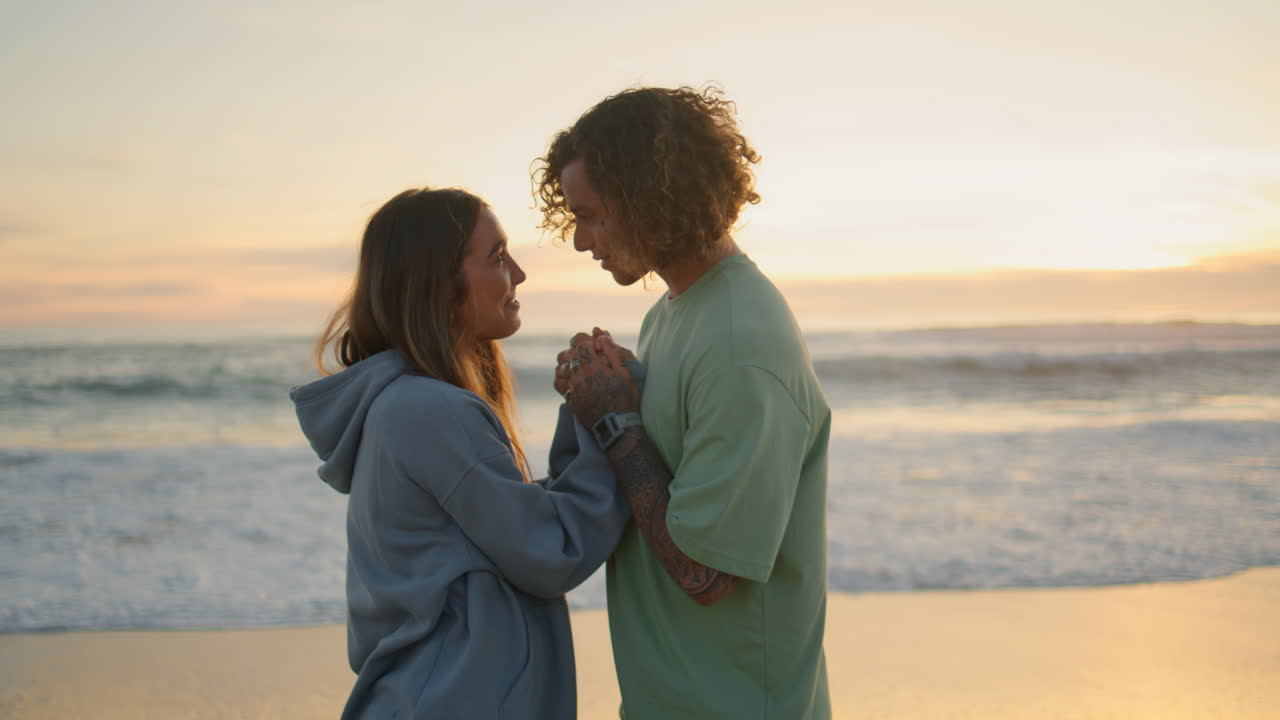 amantes jóvenes saliendo en la playa del atardecer. hombre besando manos de mujer amorosa por la noche