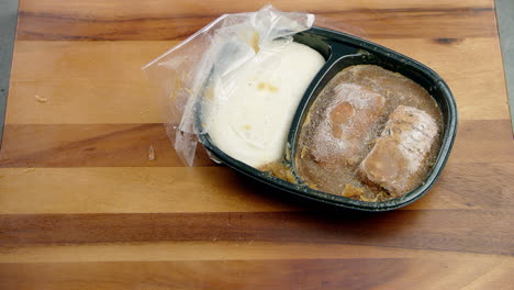 Icy-frozen-meal-food-in-a-black-container-being-dropped-sideways-on-the-dining-table