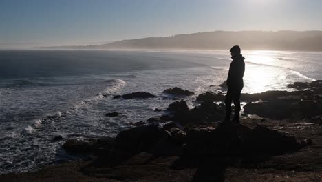 traveler man looking at the sea in pichilemu punta de lobos  chile with the sun in a sunrise watching people surf and landscape