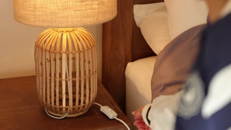 a person turns off a woven lamp on a bedside table, creating a warm, relaxed atmosphere in a cozy bedroom