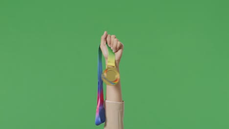 close up of business woman's hand holding a gold medal up in the air to celebrate winning as the first winner on green screen background in the studio