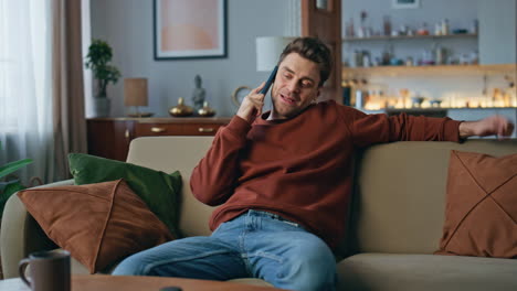 resting guy communicating smartphone at cozy couch. happy man talking cellphone