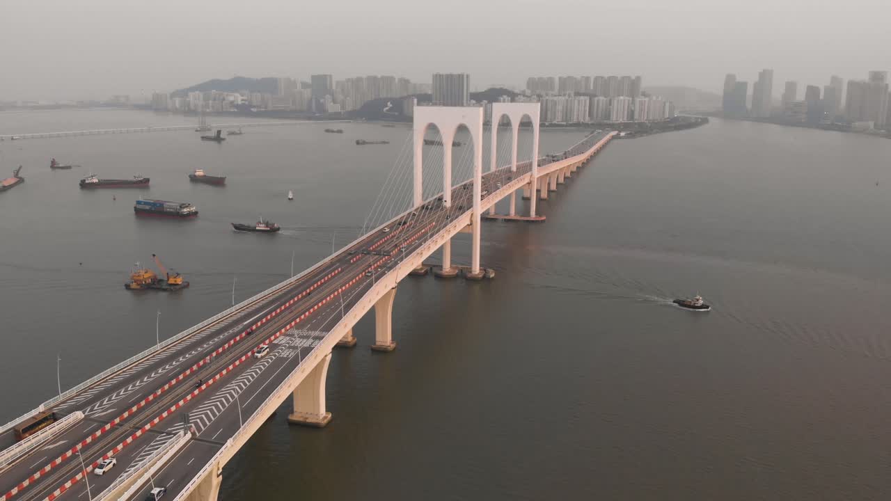 Downwards tilt and rising aerial shot of traffic crossing Sai Van Bridge in Macau with Taipa skyline as backdrop