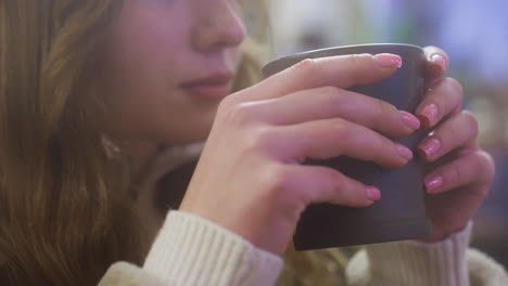 Close-up of female hand in brown shearling jacket gently lifting cup of coffee at cozy cafe table, perfect for capturing moments of relaxation, warmth, and peaceful enjoyment