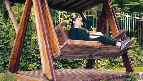 slow motion young pretty girl swinging on a wooden swing near the summer house