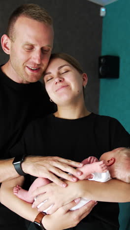 husband kisses his wife holding their newborn. happy caucasian family portrait at home. vertical video