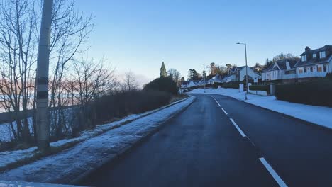 Carretera-Sinuosa-Con-Parches-De-Nieve-A-Los-Lados-Que-Conduce-A-Través-De-Un-Sereno-Paisaje-Escocés,-Cielos-Azules-Y-Claros,-Invierno,-Coche-Pov