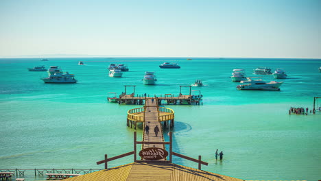 Wooden-pier-in-tourist-area-over-turquoise-water-and-moored-boats-in-the-background