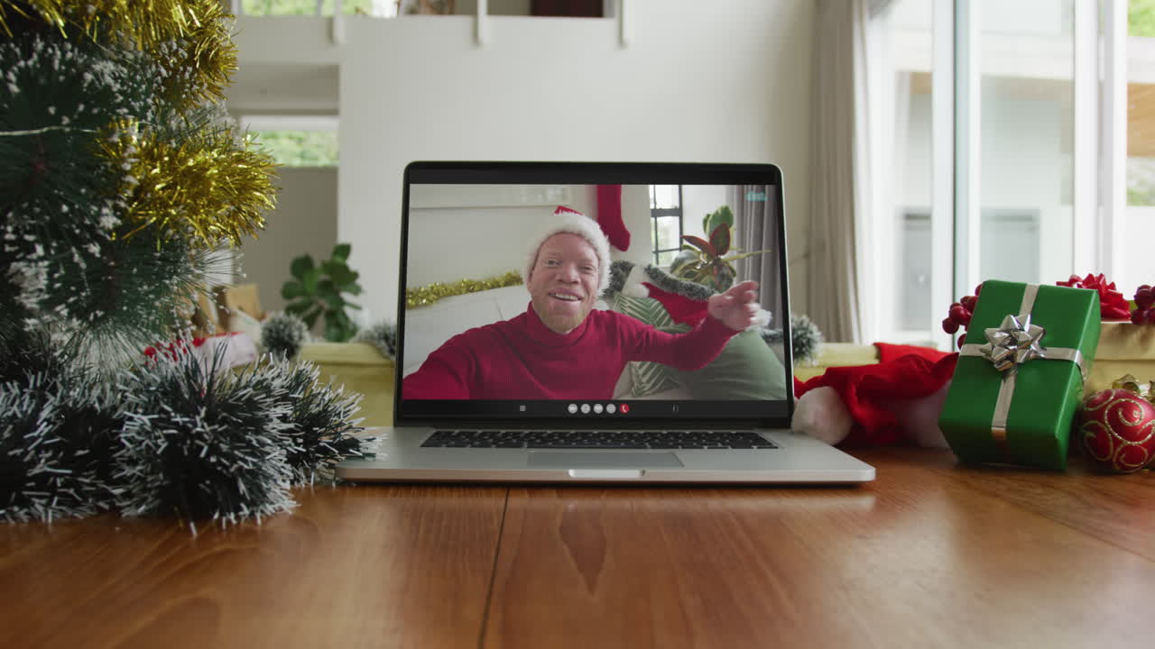 hombre afroamericano albino sonriente con sombrero de santa en una videollamada de navidad en una computadora portátil