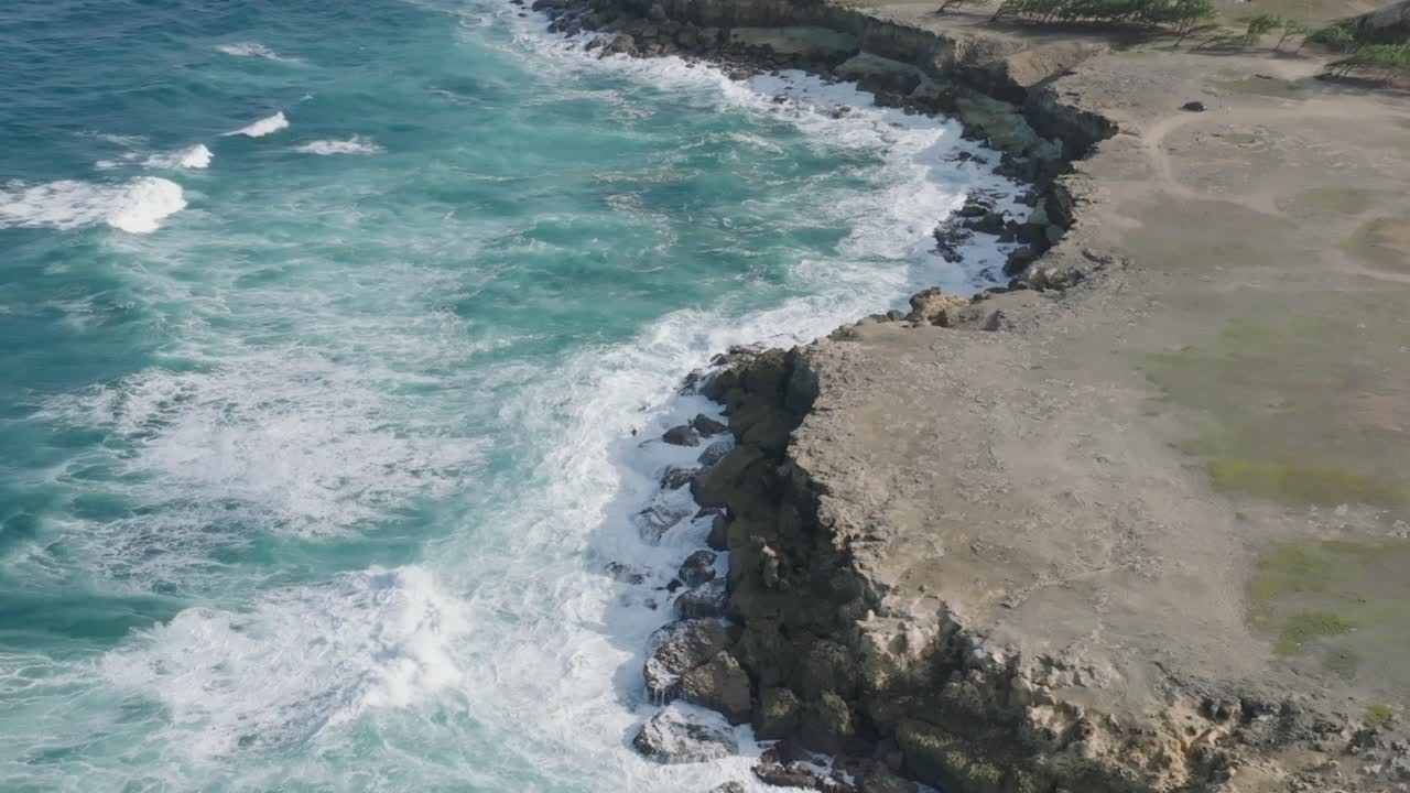 Veduta a volo d'uccello dall'alto di forti onde oceaniche che si infrangono con acqua blu turchese su una costa rocciosa.