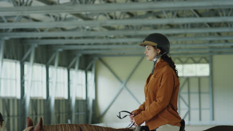a woman riding a horse in an indoor equestrian arena with an instructor