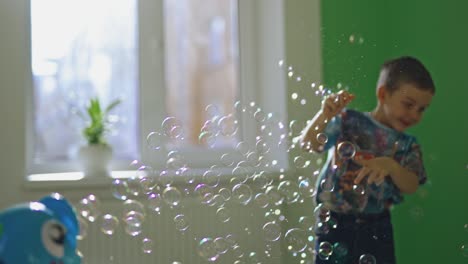 joyful boy plays with soap bubbles in his room. little child is popping colorful bubbles with his fingers and smiling at home.
