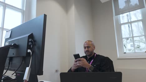 man using mobile phone in front of his computer in the office