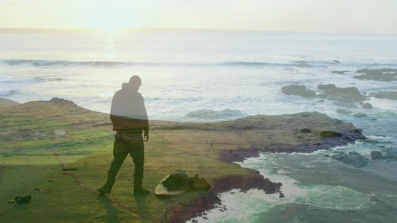 Standing on rocky shore, person silhouetted against ocean waves in background