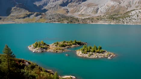 aerial view of tiny islands in the waters of lac de salanfe in valais, switzerland on a sunny autumn day in the swiss alps with a pan up view to surrounding alpine peaks and cliffs