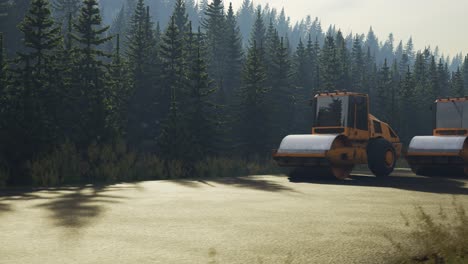 four yellow road rollers paving the asphalt road in the coniferous forest. machines working on the construction site using heavy pressure. camera moving sideways. industrial concept.