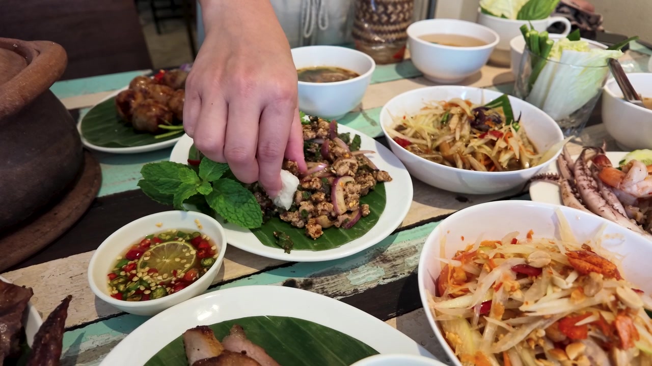 Close-up tangan mencocol nasi ketan ke dalam salad larb pedas di Bangkok, Thailand