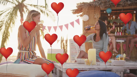 animation of red heart love balloons digital icons over friends having drinks in beach bar