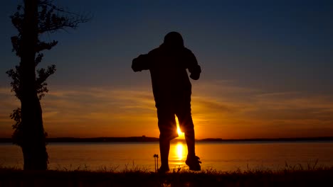 silhouette of a boy playing at sunset near a lake