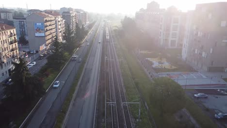 passenger train entering city of milan, aerial view fly backward with lens flare