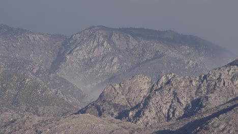 mist blowing over sunlit mountain range, static telephoto shot