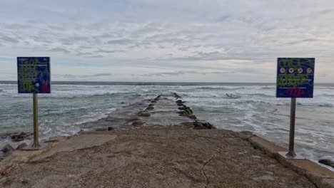 waves hitting rock pools with warning signs visible