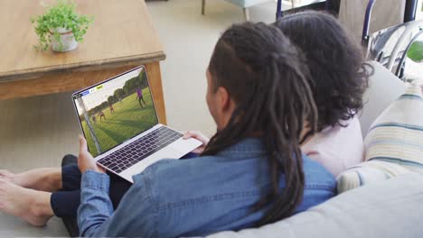 video de una pareja afroamericana sentada en el sofá y viendo fútbol en la computadora portátil en casa