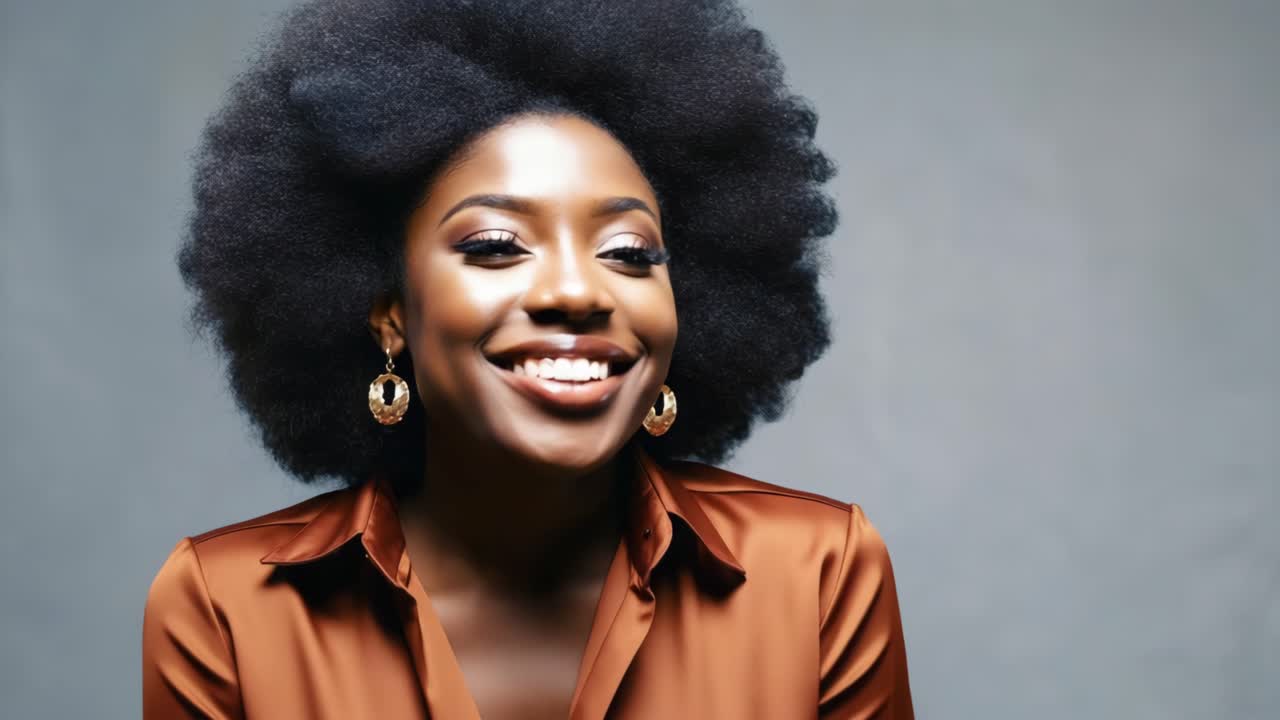 Professional businesswoman with afro hairstyle sporting brown shirt and gold earrings, standing confidently against gray background while smiling warmly and looking directly at camera