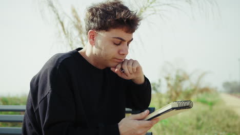 young student writing notes with a pen while on the park bench