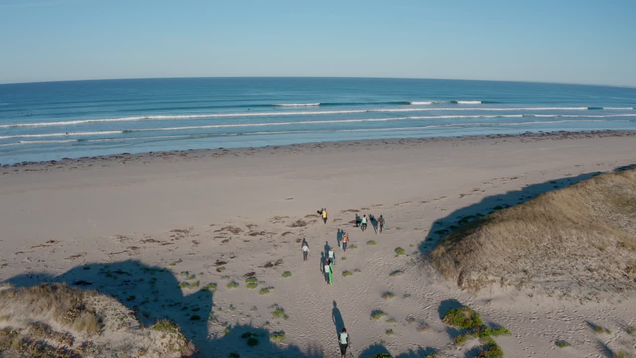 un grupo de surfistas caminando por una playa de arena hacia el océano en un día soleado