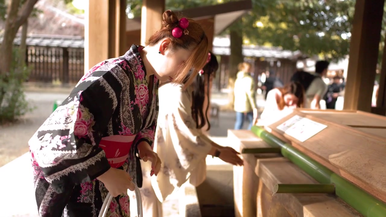 Donne in kimono floreali eseguono il tradizionale lavaggio delle mani a una fontana di purificazione di un tempio di legno.