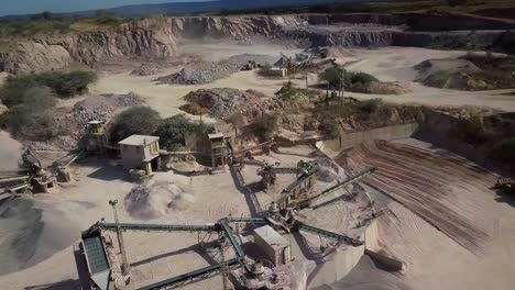 aerial-view-of-a-working-stone-quarry-with-stone-crushers,-bulldozers,-trucks-in-a-natural-environment-during-daytime