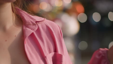 lady wearing unbuttoned pink dress places her hand with a shopping bag behind her, the background features a blurred view of glowing lights, creating a soft and radiant effect around her silhouette