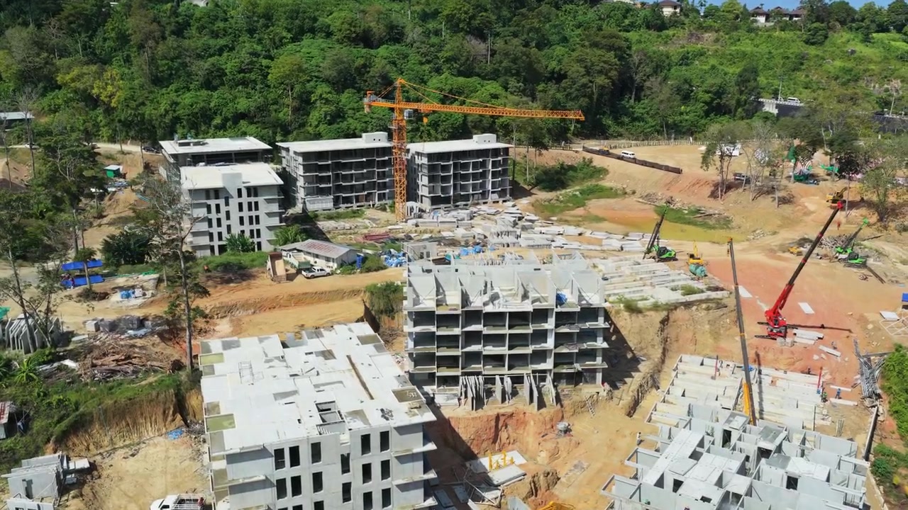 Concrete resort buildings under construction in Phuket hillside setting, drone establishing orbit