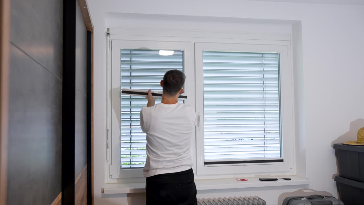 Static shot of a man carefully mounting a pleated window shade during a home DIY project in a bedroom, aligning the frame and pressing it into place for a snug fit.