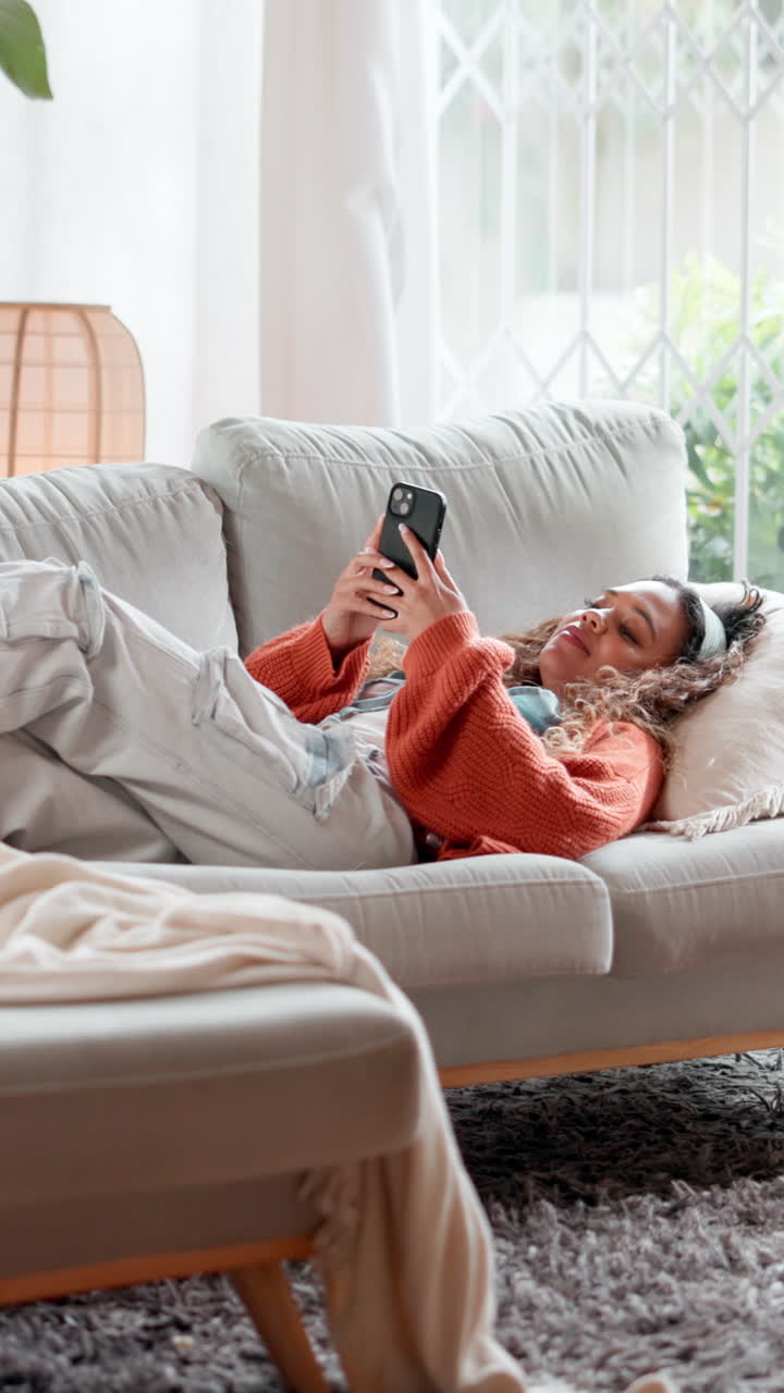 Giovane donna che si rilassa sul divano e usa lo smartphone a casa