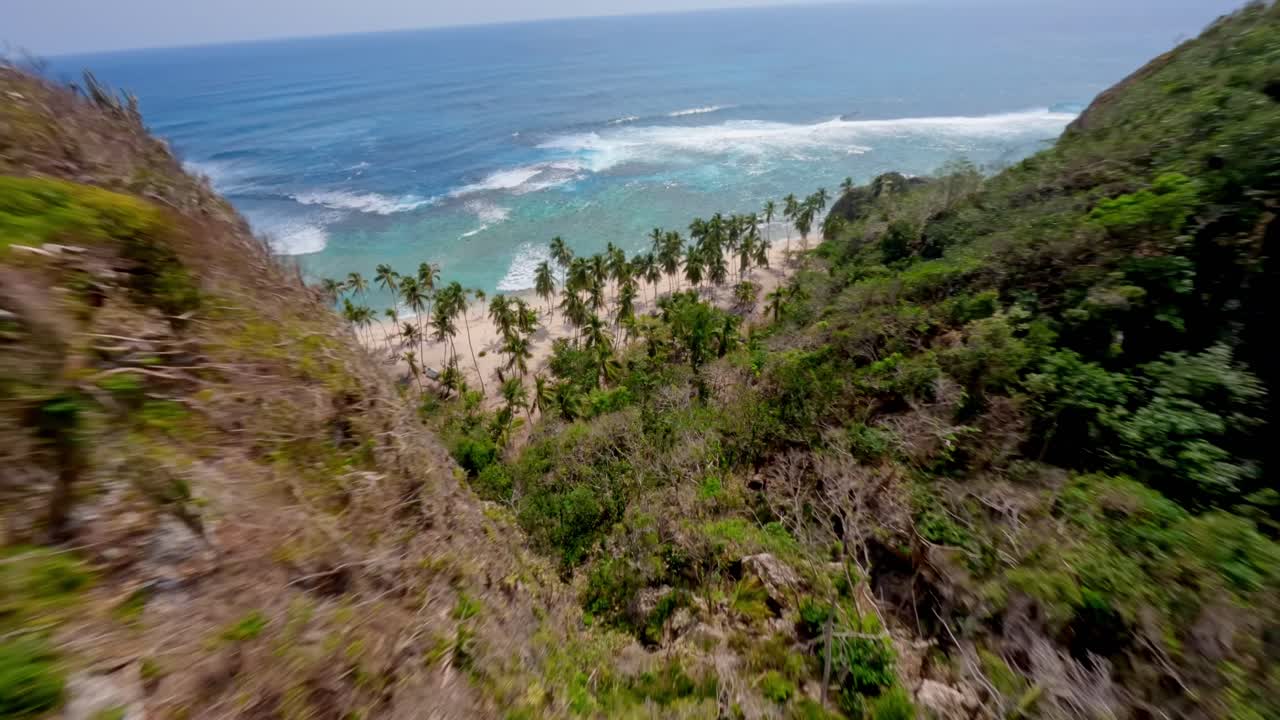 Dron letí nad rozeklanými útesy a palmami na tropické pláži Playa Frontón v Dominikánské republice
