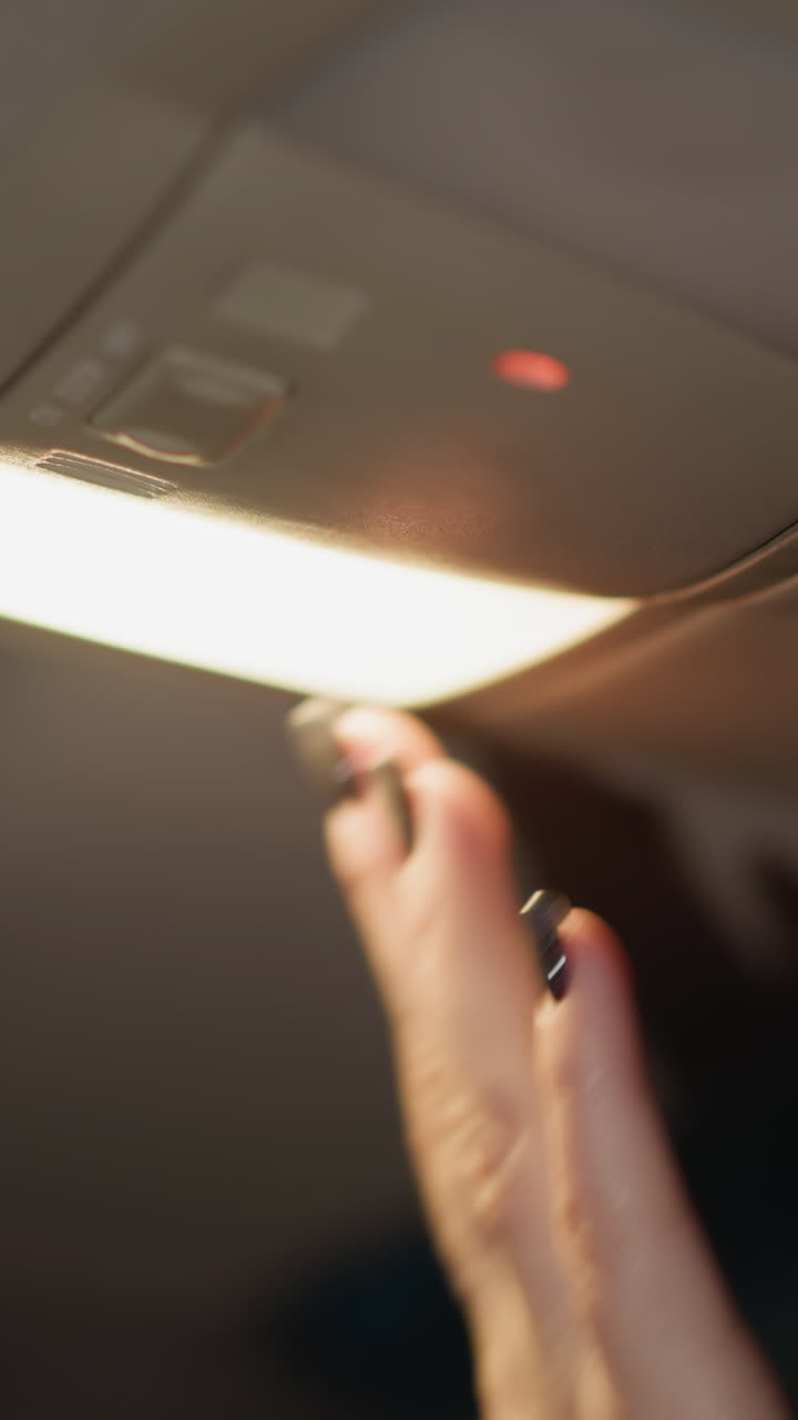 First-person view of a woman closing a car roof box and turning off the interior light at night. Hand with black painted nails interacts with the car's roof box and light switched off