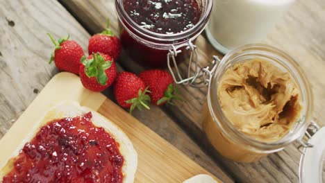 sándwich de mantequilla de maní y jalea en una bandeja de madera con leche y fresas en una superficie de madera