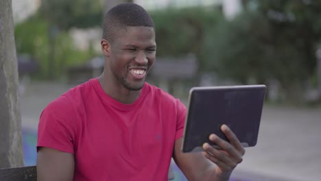 Man-watching-football-match-on-tablet-in-park,-celebrating-goal