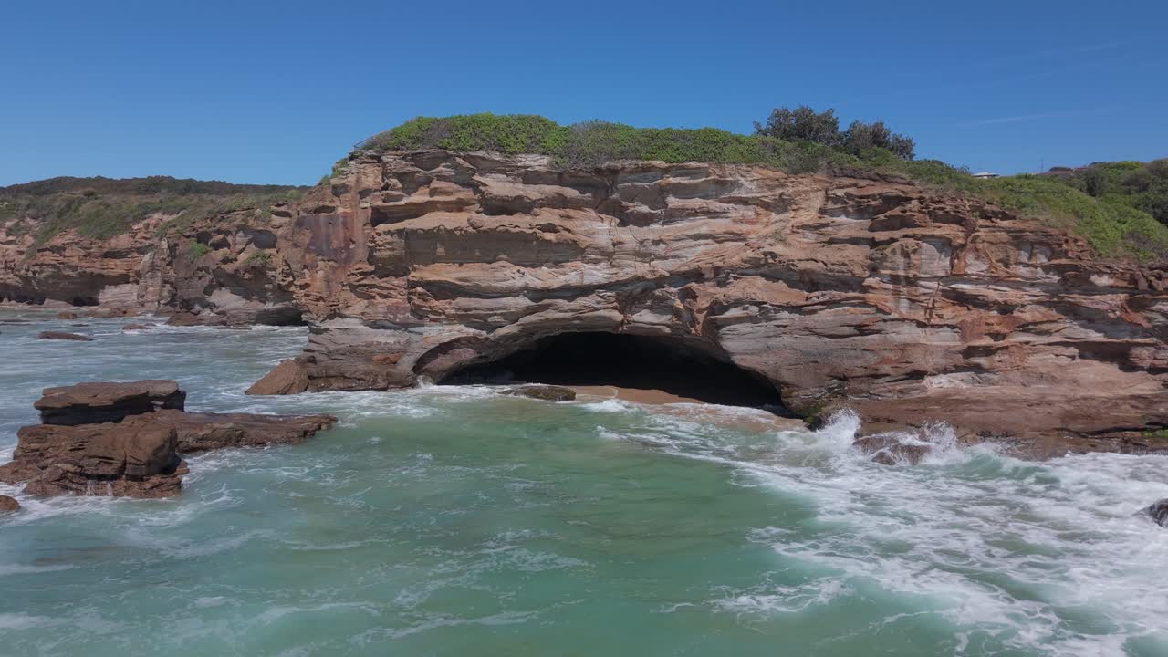 Drone pullsback over calm ocean at sunrise revealing coastal homes and surf at Caves Beach, NSW Australia