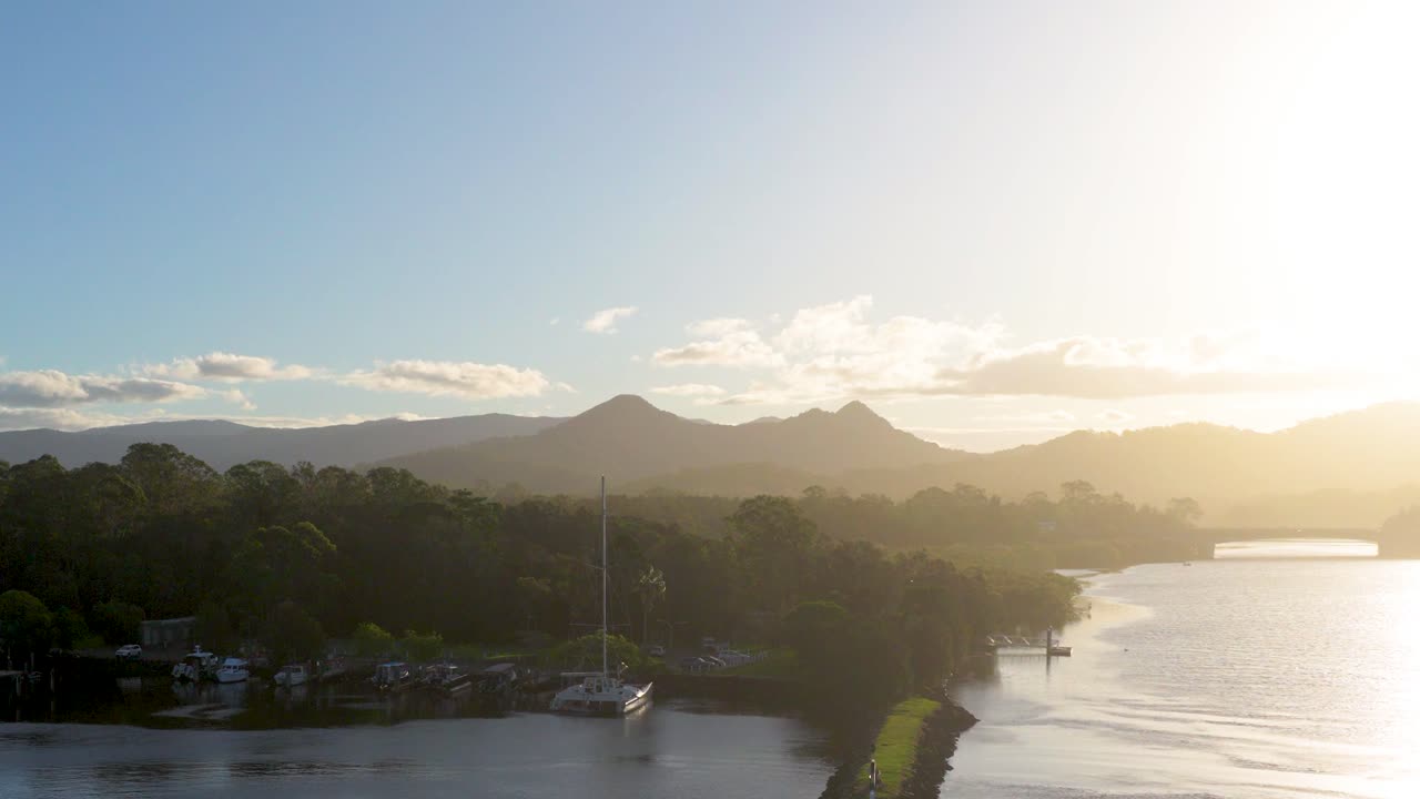 A serene sunset view over a river with distant mountains and boats, captured in Brunswick Heads, Australia